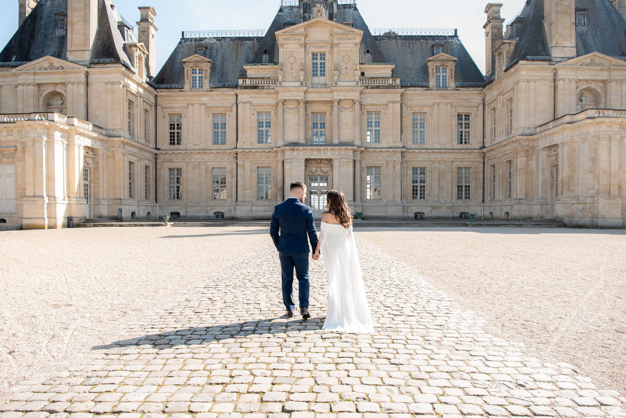 Couple de mariés marchant devant un château après leur cérémonie de mariage civil en Île-de-France.